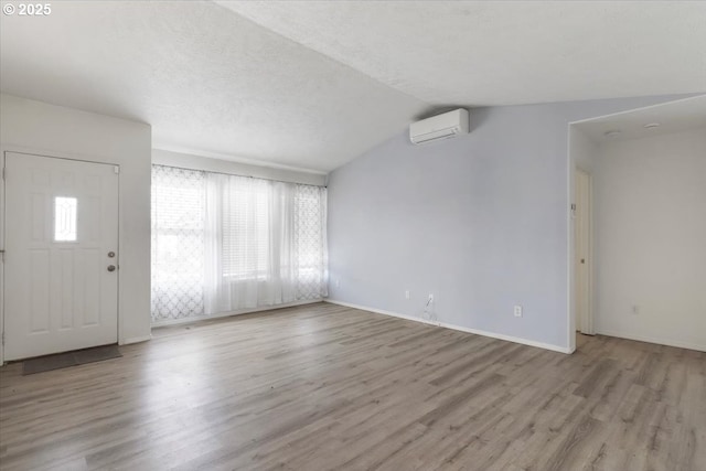 entrance foyer featuring an AC wall unit, wood finished floors, lofted ceiling, and baseboards