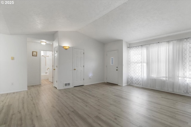 unfurnished living room featuring wood finished floors, vaulted ceiling, baseboards, and a textured ceiling