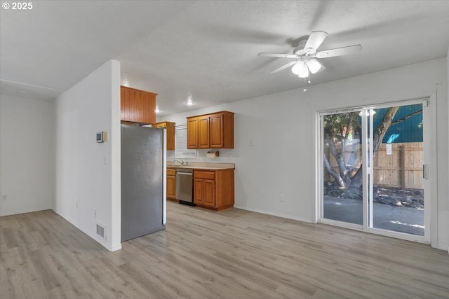 kitchen with stainless steel appliances, light wood-style flooring, brown cabinets, a ceiling fan, and light countertops