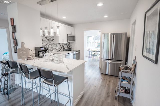 kitchen with appliances with stainless steel finishes, tasteful backsplash, light wood-style floors, a peninsula, and a sink