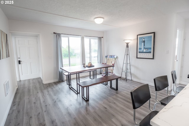 dining area with baseboards, light wood-type flooring, and a textured ceiling