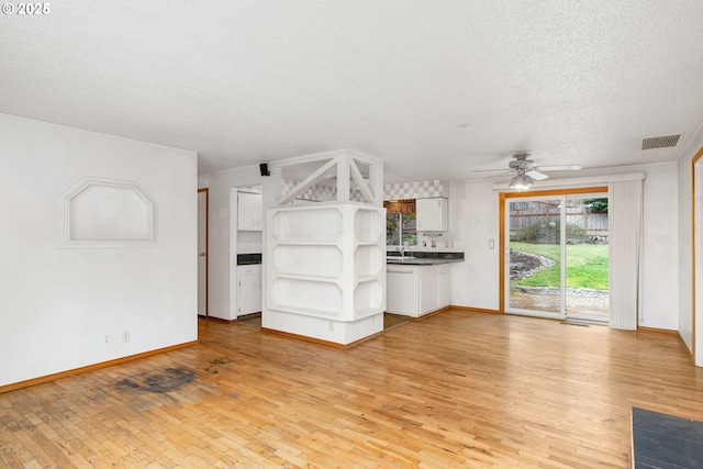 unfurnished living room with light wood finished floors, visible vents, a textured ceiling, a ceiling fan, and a sink