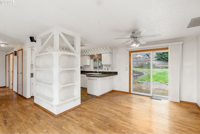 kitchen with visible vents, a peninsula, light wood-style flooring, open shelves, and dark countertops