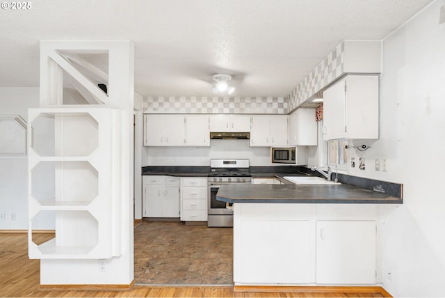 kitchen with a sink, under cabinet range hood, dark countertops, white cabinetry, and stainless steel appliances