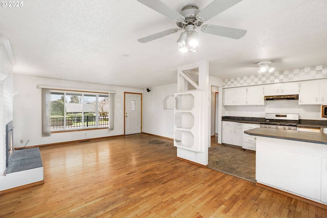 kitchen featuring dark countertops, under cabinet range hood, gas range, light wood-style floors, and white cabinets