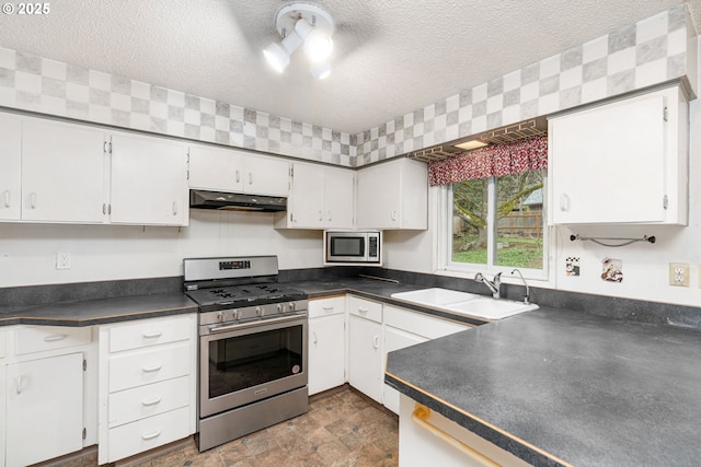 kitchen featuring under cabinet range hood, dark countertops, appliances with stainless steel finishes, and a sink