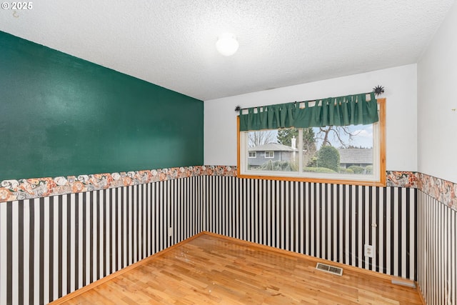 spare room featuring visible vents, a textured ceiling, and a wainscoted wall