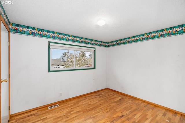 empty room featuring visible vents, light wood-type flooring, and baseboards