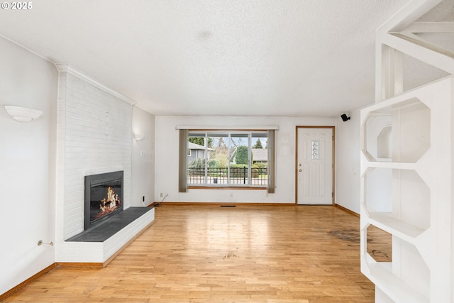 unfurnished living room with a brick fireplace, a textured ceiling, and light wood-type flooring