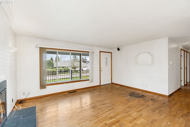 unfurnished living room featuring visible vents, a fireplace with flush hearth, hardwood / wood-style flooring, a textured ceiling, and baseboards