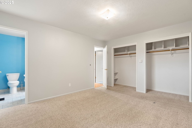 unfurnished bedroom with carpet floors, connected bathroom, a textured ceiling, and two closets