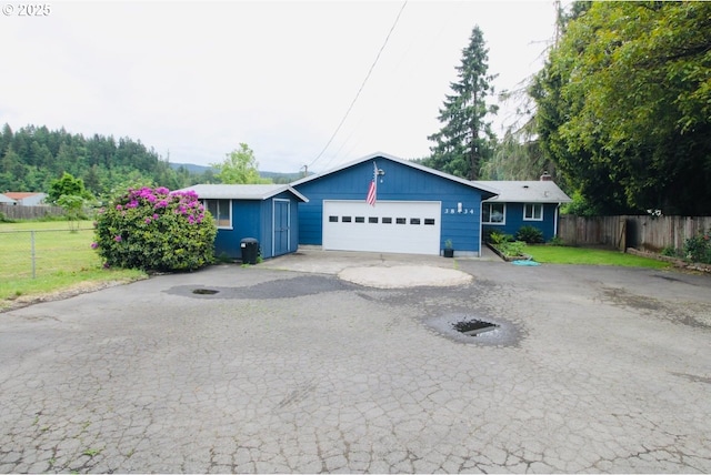 ranch-style home featuring a garage, driveway, an outdoor structure, and a storage unit