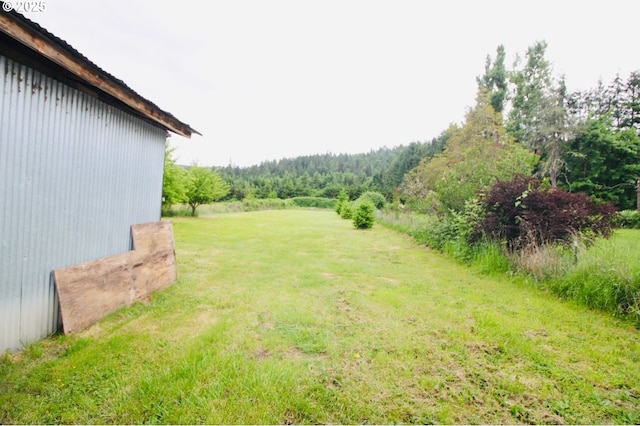 view of green lawn featuring a wooded view
