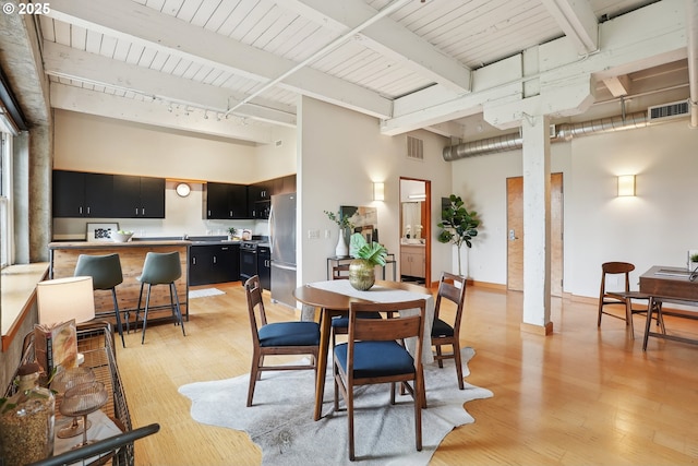 dining area with light wood finished floors, a high ceiling, and beam ceiling