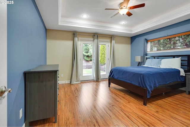 bedroom with access to exterior, light wood-style flooring, a ceiling fan, baseboards, and a tray ceiling