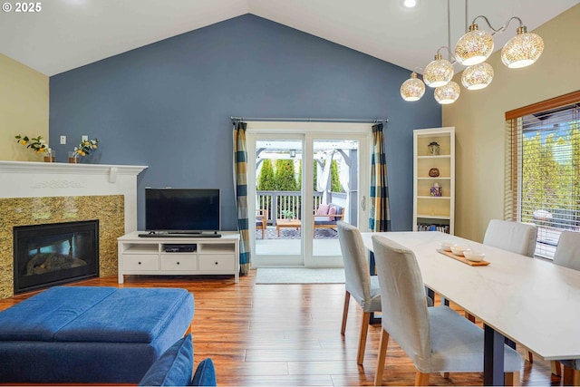 dining space with wood finished floors, high vaulted ceiling, recessed lighting, a high end fireplace, and a chandelier