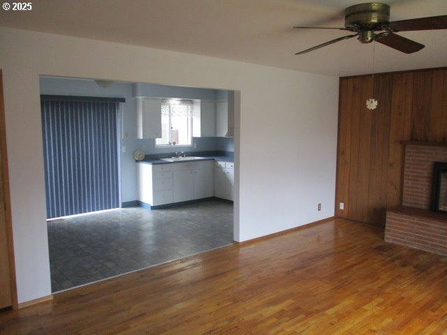 1210 Alder St, Elgin, OR 97827 - unfurnished living room with a ceiling fan, a fireplace, wood walls, wood finished floors, and a sink