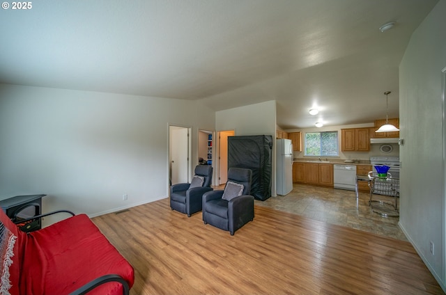 living room featuring visible vents, baseboards, lofted ceiling, light wood-style flooring, and a wood stove