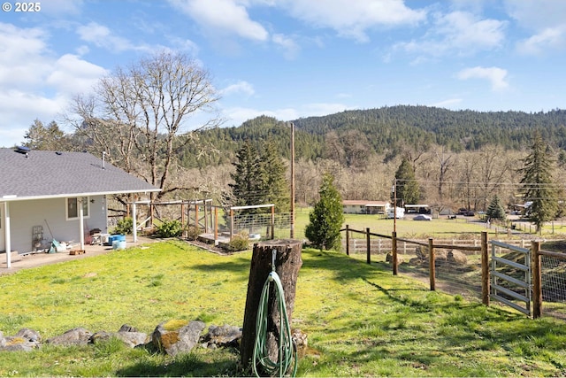 view of yard with a garden, a wooded view, and fence