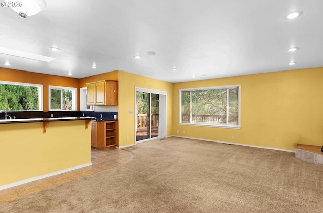 kitchen with recessed lighting, a sink, light carpet, a kitchen bar, and dark countertops