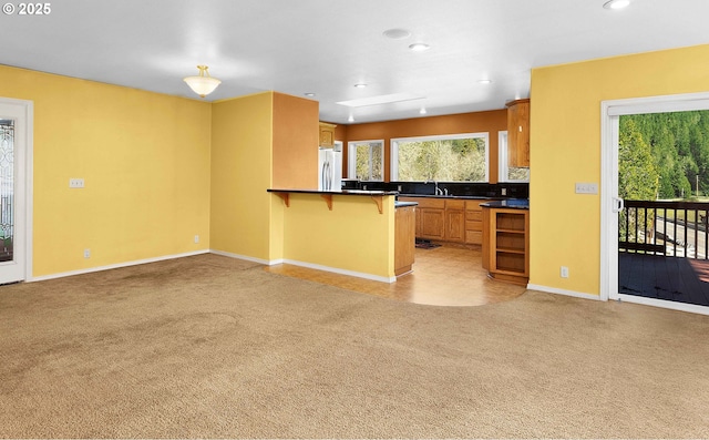 kitchen featuring a peninsula, freestanding refrigerator, light carpet, dark countertops, and a kitchen breakfast bar