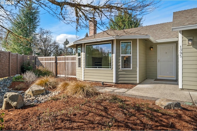 entrance to property with fence, roof with shingles, and a chimney