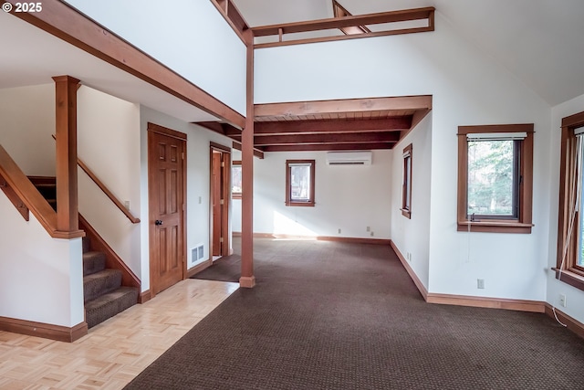 interior space with a towering ceiling, light parquet flooring, a wall mounted AC, decorative columns, and beam ceiling