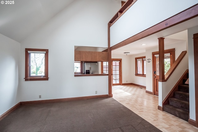 unfurnished living room featuring high vaulted ceiling, light parquet flooring, and decorative columns