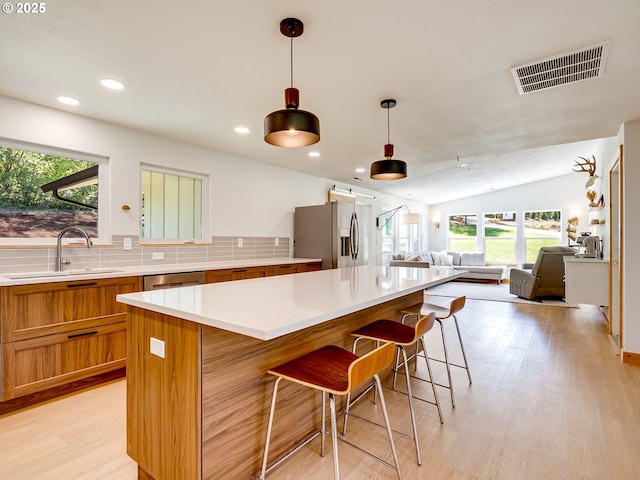 kitchen with visible vents, brown cabinets, open floor plan, stainless steel appliances, and light wood-style flooring