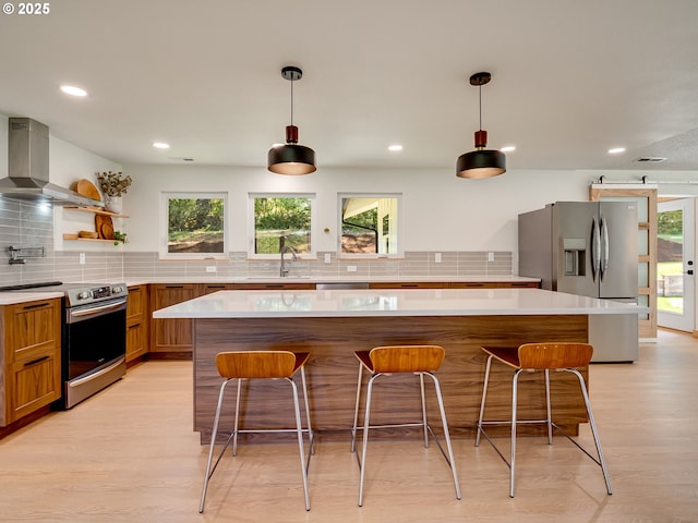kitchen with backsplash, a healthy amount of sunlight, wall chimney range hood, and stainless steel appliances