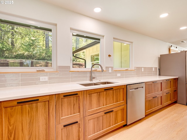 kitchen featuring a sink, light wood-style floors, light countertops, stainless steel appliances, and decorative backsplash