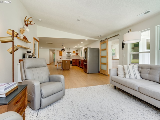 living room with visible vents, a barn door, light wood-style flooring, and lofted ceiling