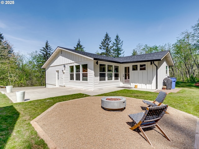 back of house with board and batten siding, a lawn, a shingled roof, a patio area, and a fire pit