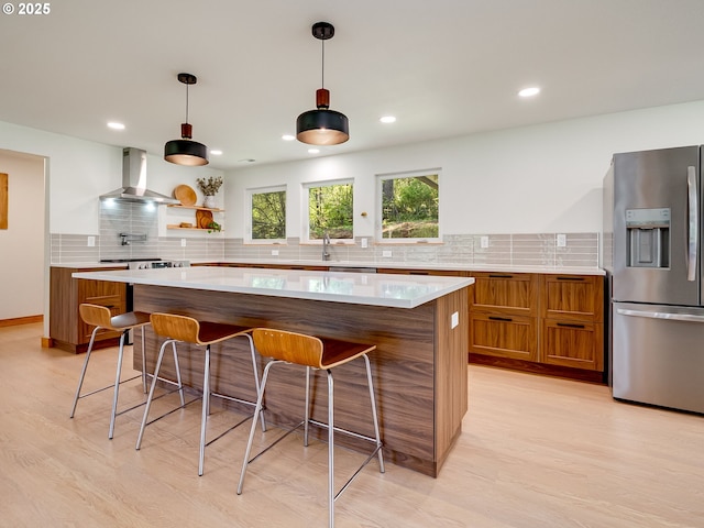 kitchen featuring wall chimney exhaust hood, backsplash, brown cabinets, and stainless steel fridge with ice dispenser