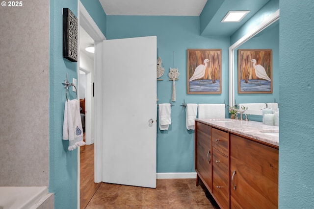 full bathroom with double vanity, a sink, a bath, and baseboards