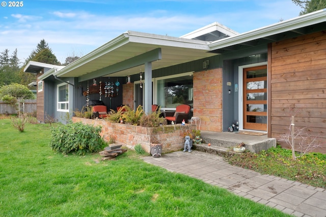 entrance to property featuring covered porch, a yard, and fence