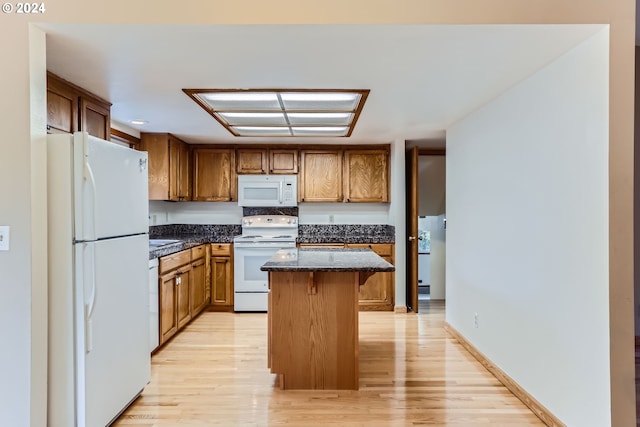 kitchen with brown cabinetry, white appliances, a breakfast bar area, light wood-type flooring, and a kitchen island
