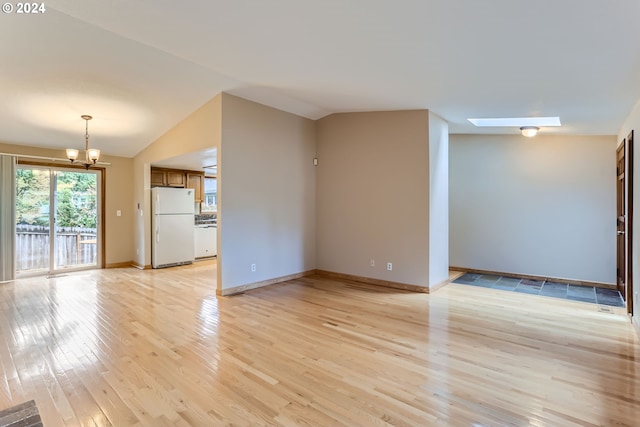 unfurnished living room featuring baseboards, a notable chandelier, vaulted ceiling with skylight, and light wood-type flooring