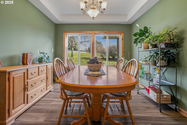 dining area with a raised ceiling, hardwood / wood-style floors, and an inviting chandelier