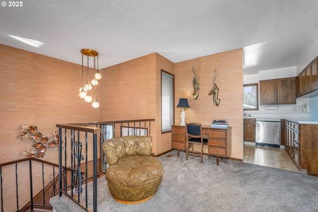 kitchen with a textured ceiling, stainless steel dishwasher, carpet flooring, and hanging light fixtures