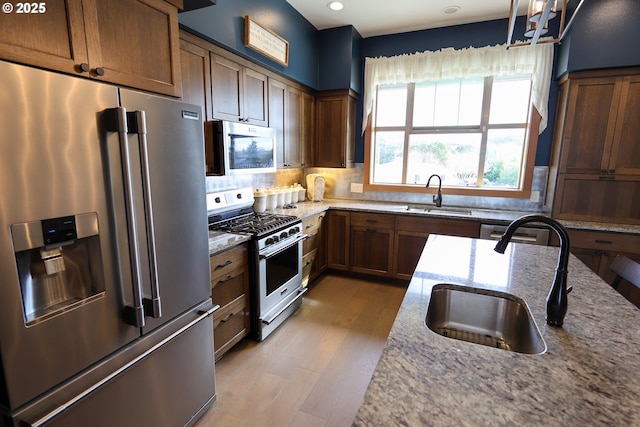 kitchen featuring appliances with stainless steel finishes, light wood-style flooring, a sink, and light stone counters