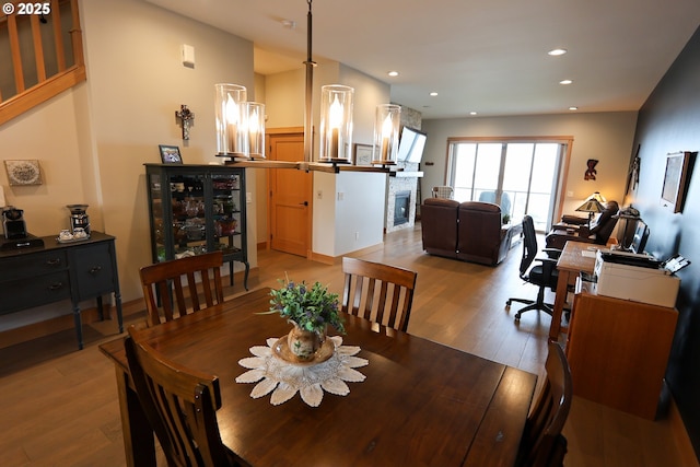 dining space with light wood-style flooring, a stone fireplace, and recessed lighting