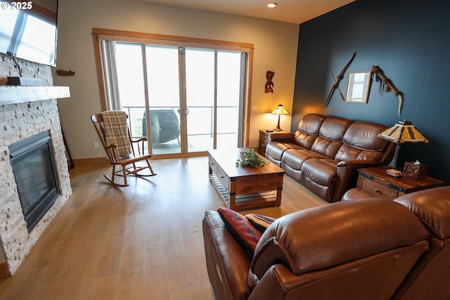 living room with a healthy amount of sunlight, light wood finished floors, baseboards, and a stone fireplace