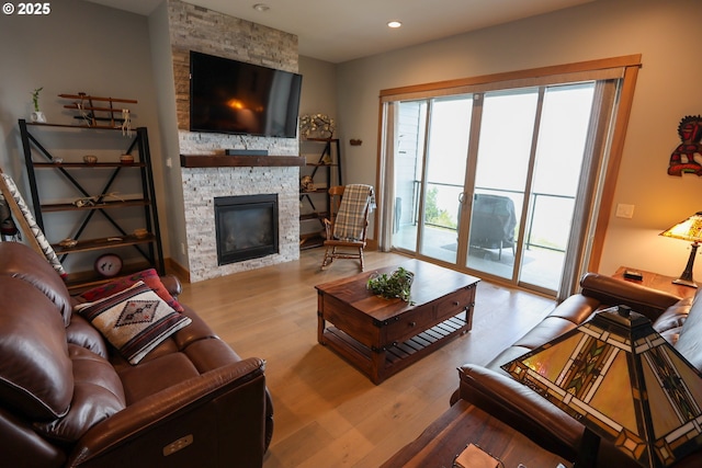 living area featuring recessed lighting, a stone fireplace, and wood finished floors