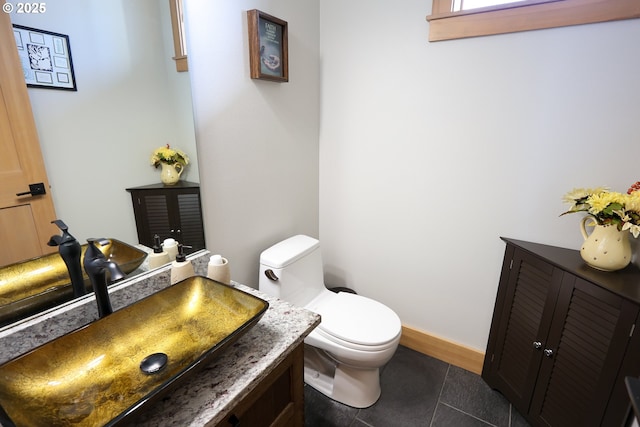 half bathroom with tile patterned flooring, baseboards, vanity, and toilet