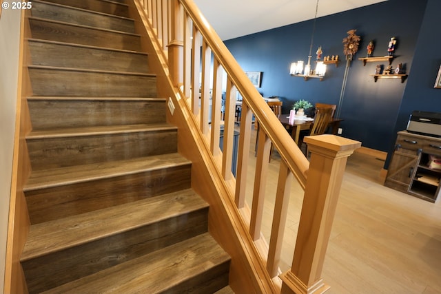 stairs featuring wood finished floors and an inviting chandelier