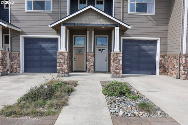 doorway to property featuring a garage, concrete driveway, and stone siding