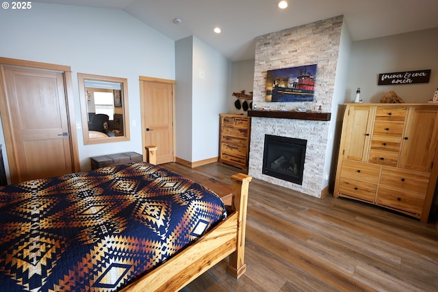 bedroom featuring baseboards, wood finished floors, vaulted ceiling, a fireplace, and recessed lighting