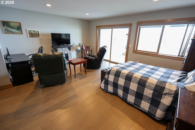 bedroom with light wood finished floors, access to outside, a stone fireplace, and recessed lighting