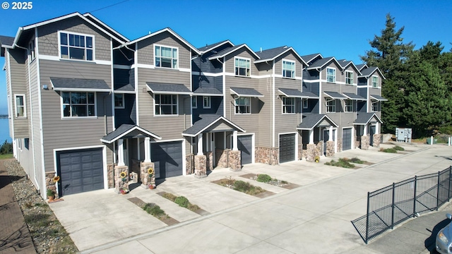 townhome / multi-family property featuring a garage, a residential view, stone siding, and driveway